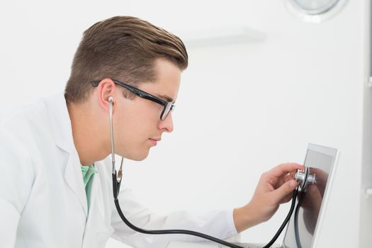 Technician listening to laptop with stethoscope in his office