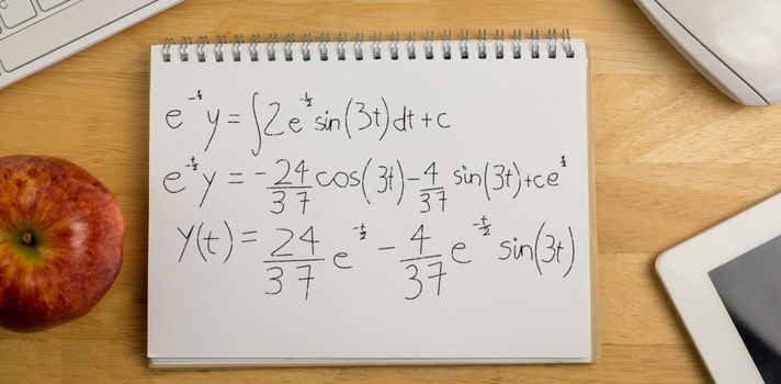 Calculations against black background against overhead of notepad and technology 