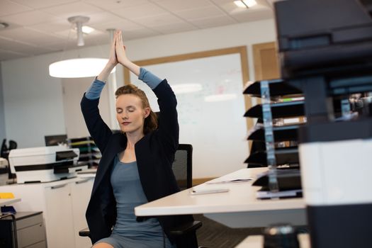 Businesswoman practicing yoga while sitting on chair by desk at office