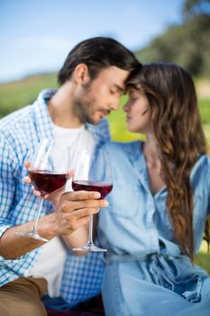 Romantic young couple holding red wine glasses with vineyard in background