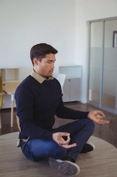 Young businessman practicing yoga while sitting on desk at office