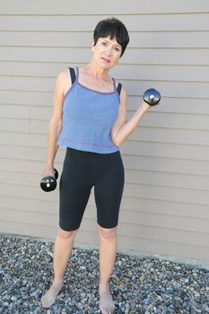 Mature female beauty working out with hand weights outside.