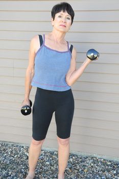 Mature female beauty working out with hand weights outside.