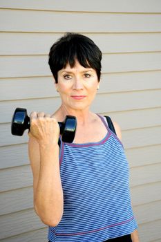 Mature female beauty working out with hand weights outside.