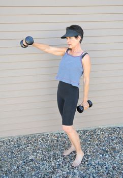 Mature female beauty working out with hand weights outside.