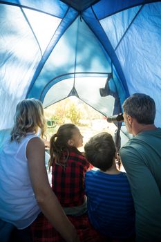 Rear view of family looking through telescope while sitting in the tent