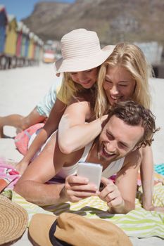 Happy family taking selfie while lying on picnic blanket at beach during sunny day