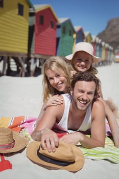 Portrait of happy family lying together on blanket at beach during sunny day