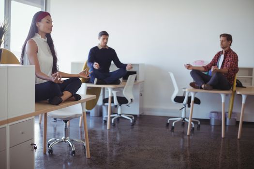 Business people practicing yoga while sitting on desk at office
