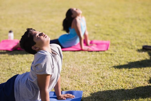 Boy and girl practicing yoga on exercise mat at park