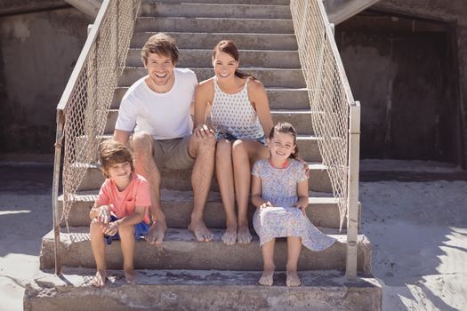 Smiling family sitting on staircase during sunny day