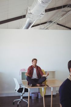 Young businessman doing yoga while sitting on desk at office