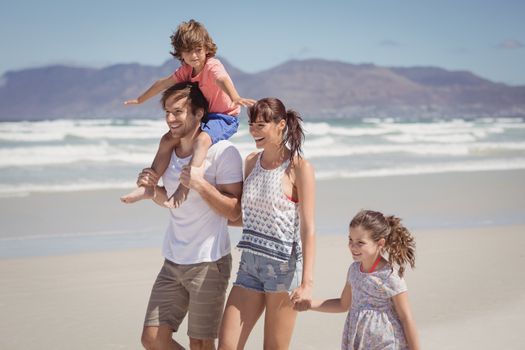 Happy family walking at beach during sunny day