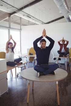 Young business people doing yoga while sitting on desk at office