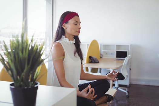 Young businesswoman doing yoga while sitting on desk at office