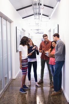 Business people using technologies while standing in corridor 