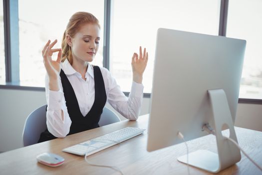 Beautiful executive performing yoga at desk in office