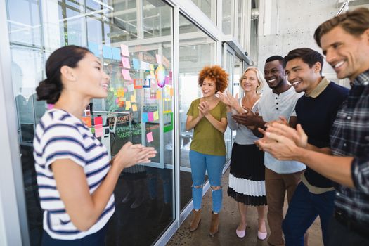 Happy business people applauding while standing against plan on glass wall in office