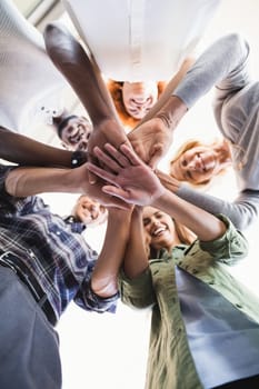 Directly below portrait of smiling business people stacking hands while standing in office