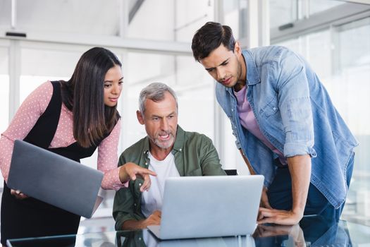 Business people discussing over laptops at desk in office