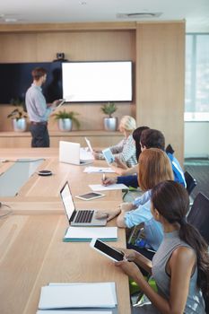 Business people using laptop and digital tablets at conference table during meeting in board room