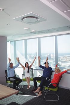 Cheerful business people with arms raised sitting on chairs by window at office