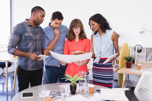 Business people discussing over paper while standing at desk in office