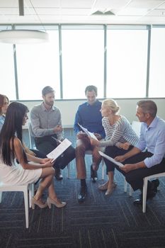 Business people discussing over documents while sitting on chairs at office