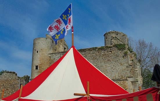 Top of medieval red and white tent with normandy flag at top and castle in background