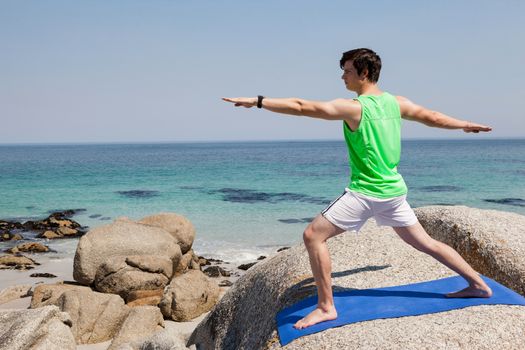 Man performing yoga on rock near the coast