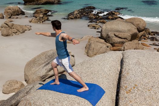 Man performing yoga on rock near the coast