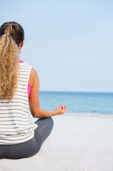 Rear view of young woman practicing yoga at beach against clear blue sky on sunny day