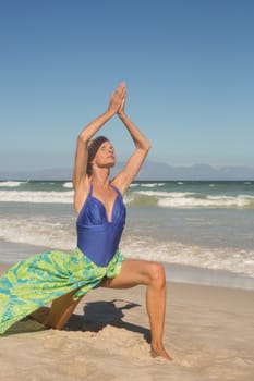 Woman with arms raised practising yoga against clear sky at beach
