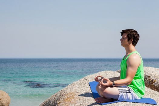 Man performing yoga on rock near the coast