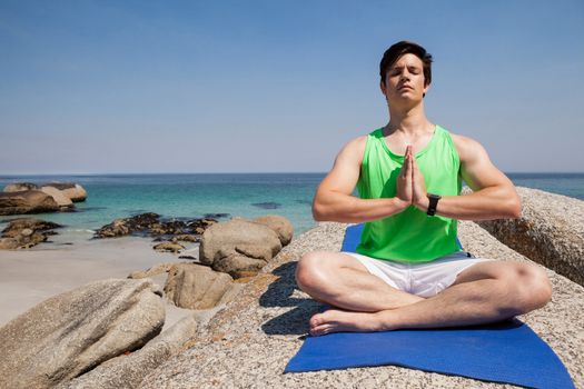 Man performing yoga on rock near the coast