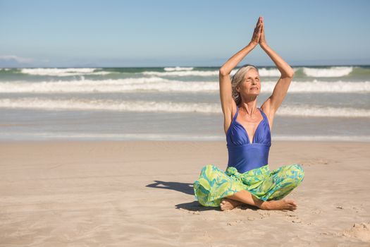 Senior woman practising yoga while sitting against clear sky at beach