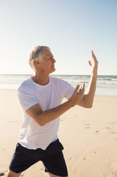 Active senior man practicing yoga at beach during sunny day