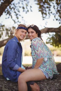 Side view portrait of smiling romantic couple sitting on tree trunk at forest