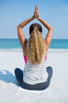 Rear view of woman practicing yoga while sitting at beach against clear blue sky