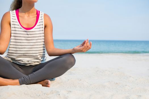 Low section of woman practicing yoga at beach against clear blue sky on sunny day