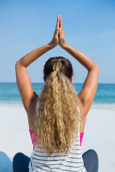 Rear view of woman practicing yoga at beach against clear blue sky