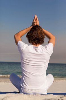 Rear view of man performing yoga at beach on a sunny day