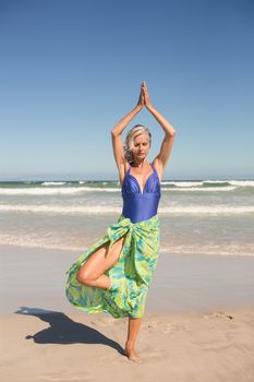 Senior woman practising yoga while standing against sea at beach