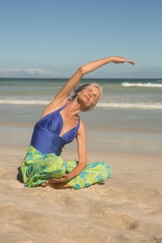 Close up of woman practising yoga while sitting on sand at beach