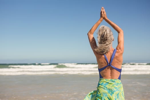 Rear view of woman practising yoga while standing at beach