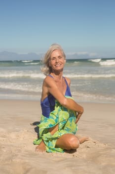 Portrait of smiling woman practising yoga while sitting on sand at beach