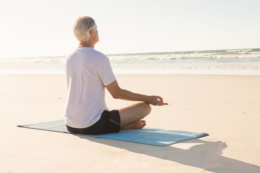 Senior man doing yoga at beach on sunny day
