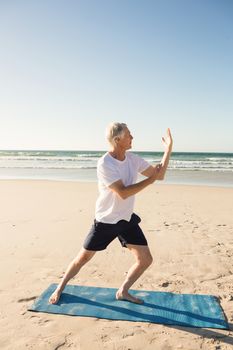 Full length of active senior man practicing yoga at beach during sunny day