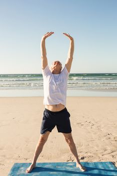 Full length of senior man practicing yoga at beach on sunny day