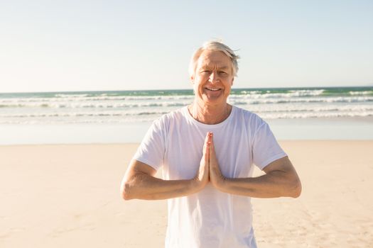 Portrait of happy senior man doing yoga at beach on sunny day